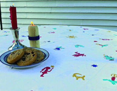 A table decorated by stenciling with candles and a plate of cookies on the table.